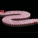 Strands of light pink rose quartz beads are arranged in an elegant curve across a glossy black background. The soft pink thread running through the beads is slightly visible, complementing their natural hue.