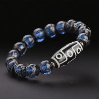 This elegant bracelet pairs a black and white 9-eye Dzi bead with a sequence of deep blue marbled beads, featuring faint metallic streaks. Set against a black background, the piece gives off a refined yet powerful spiritual presence.