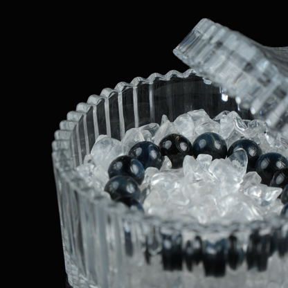 A close-up of a crystal bracelet surrounded by clear quartz chips inside a ridged glass container.