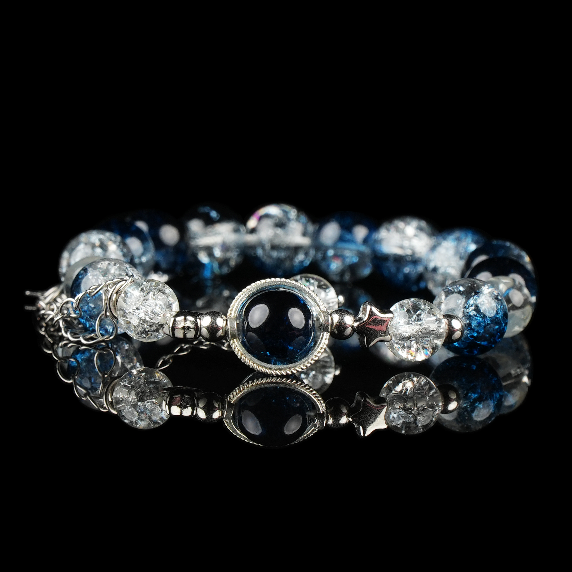 A celestial-inspired bracelet featuring galaxy energy beads in deep blue and crackled clear tones, accented with silver star spacers and a central orb framed in silver. The reflective black surface enhances its cosmic and mystical aesthetic.