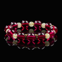 A vibrant bracelet composed of deep red garnet and golden quartz beads, accented with gold-toned spacers, resting elegantly on a glossy black background with mirror reflection.