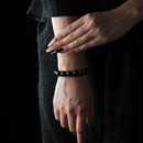 A woman dressed in black wearing a bracelet made of gold sheen obsidian beads, which reflect a subtle metallic shimmer under the light, exuding a mysterious and elegant aura.
