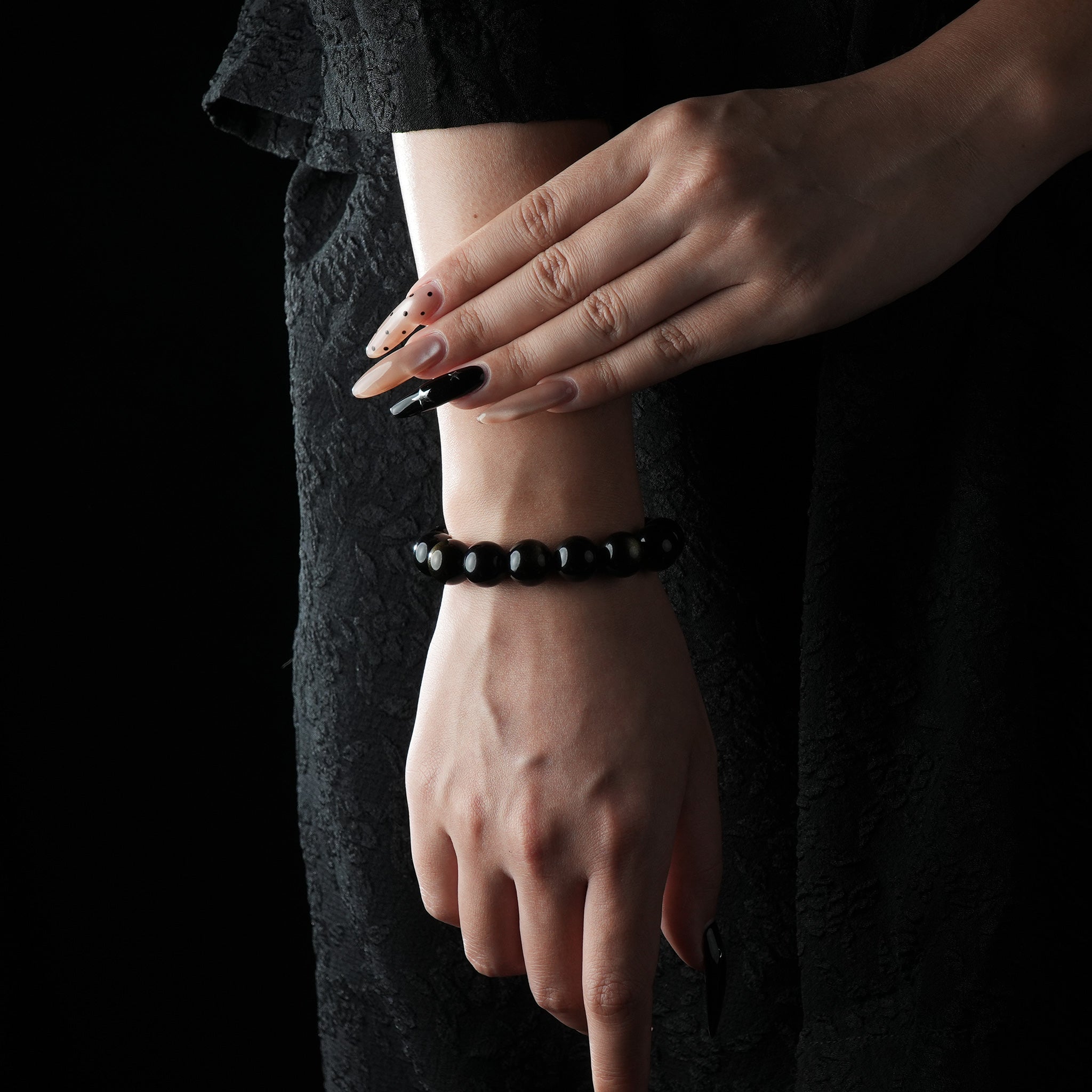 A woman dressed in black wearing a bracelet made of gold sheen obsidian beads, which reflect a subtle metallic shimmer under the light, exuding a mysterious and elegant aura.