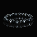 Close-up view of a gold sheen obsidian bracelet featuring polished black beads with subtle golden highlights, displayed on a black reflective background to emphasize its sleek, protective energy.