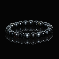 Close-up view of a gold sheen obsidian bracelet featuring polished black beads with subtle golden highlights, displayed on a black reflective background to emphasize its sleek, protective energy.