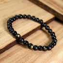 Beaded bracelet placed diagonally on wooden steps, highlighting the contrast between smooth black and golden shimmer stones for a sense of calm power.
