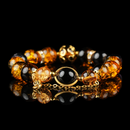 A luxurious bracelet featuring galaxy-inspired energy beads in rich amber and deep black, accented with gold detailing and a central black orb framed in gold. The high-gloss black background highlights the bracelet's celestial elegance and radiant glow.