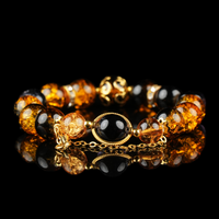 A luxurious bracelet featuring galaxy-inspired energy beads in rich amber and deep black, accented with gold detailing and a central black orb framed in gold. The high-gloss black background highlights the bracelet's celestial elegance and radiant glow.