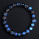 High-resolution top-down shot of a gray moonstone bracelet on a dark surface, where vibrant blue reflections dance across the translucent gray beads.