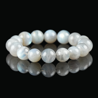 Flat lay of gray moonstone bracelet with round beads showing soft bluish sheen on black reflective background – used for calming energy.