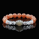 A beaded bracelet made of shimmering gray moonstone at the center, flanked by clear quartz and warm orange moonstone beads, displayed on a black reflective surface, held gracefully by hand, and elegantly worn on the wrist.