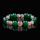 A handmade bracelet featuring alternating glossy green agate and soft pink strawberry quartz beads, laid out in a circular arrangement on a reflective black surface.