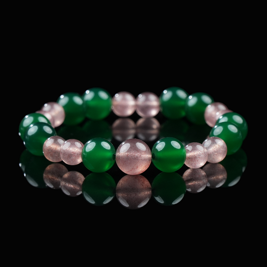 A handmade bracelet featuring alternating glossy green agate and soft pink strawberry quartz beads, laid out in a circular arrangement on a reflective black surface.