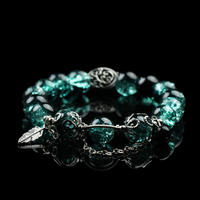 Emerald green cracked energy bead bracelet with black accent beads, silver feather charm, and chain detail, styled on a glossy black background for a bold natural look.