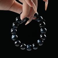 A bracelet composed of glossy blue tiger eye beads held against a dark background, highlighting their natural luster and flowing light reflections.