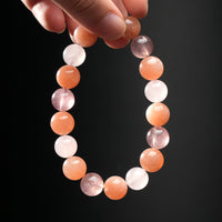 Close-up of hand holding Cancer zodiac crystal bracelet made with calming moonstone, nurturing strawberry quartz, and energizing sunstone.
