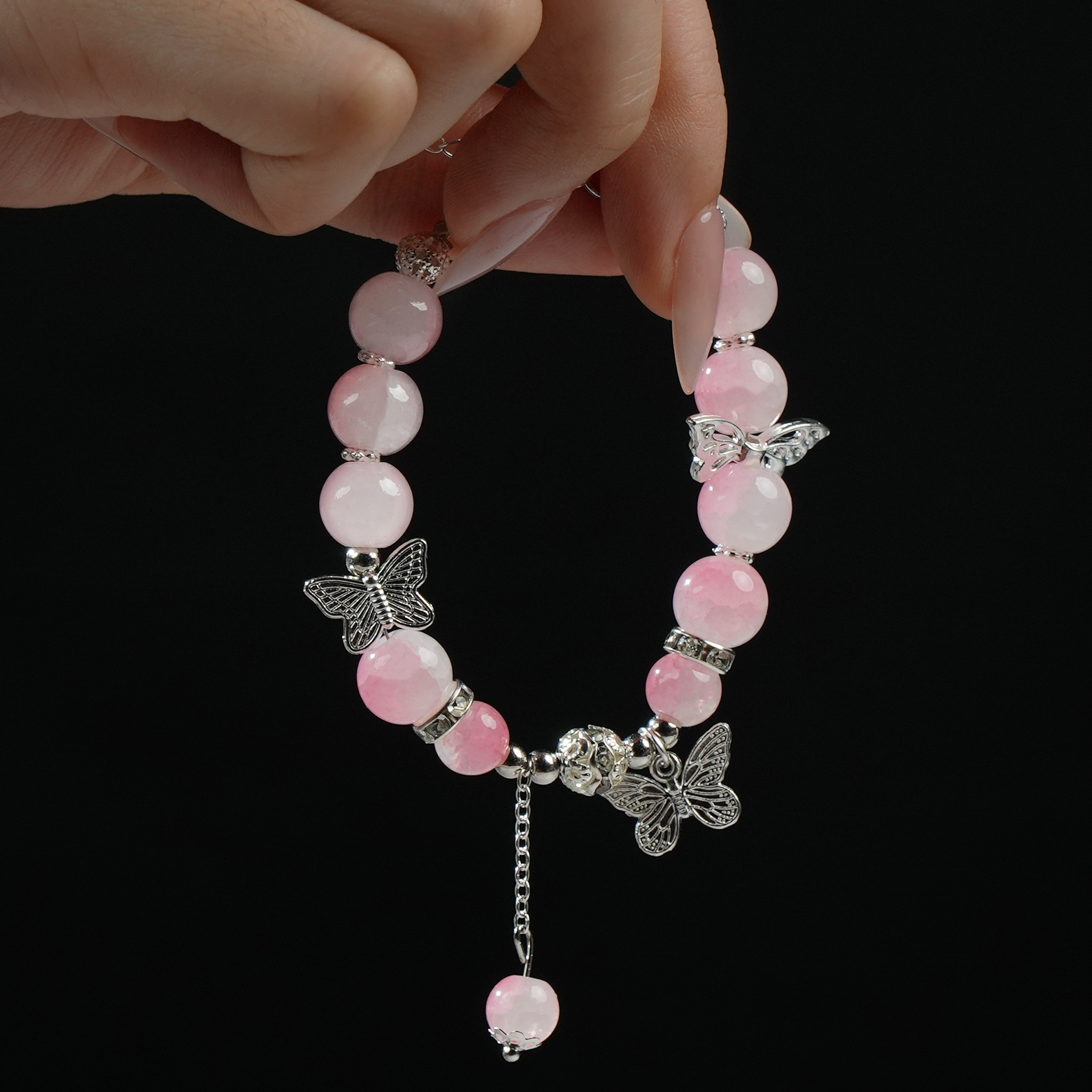 A hand gracefully presenting a handmade rose quartz bracelet with butterfly charms and healing energy beads, ideal for love and transformation rituals.
