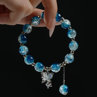 A hand holding a gradient blue energy bead bracelet with a crystal-clear butterfly charm—evoking the serenity and vastness of the sky.