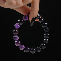 A hand gracefully pinching the top of a beautifully strung bracelet made of polished Amethyst and Blue Goldstone gemstones, showcasing their rich sparkle and glossy finish.