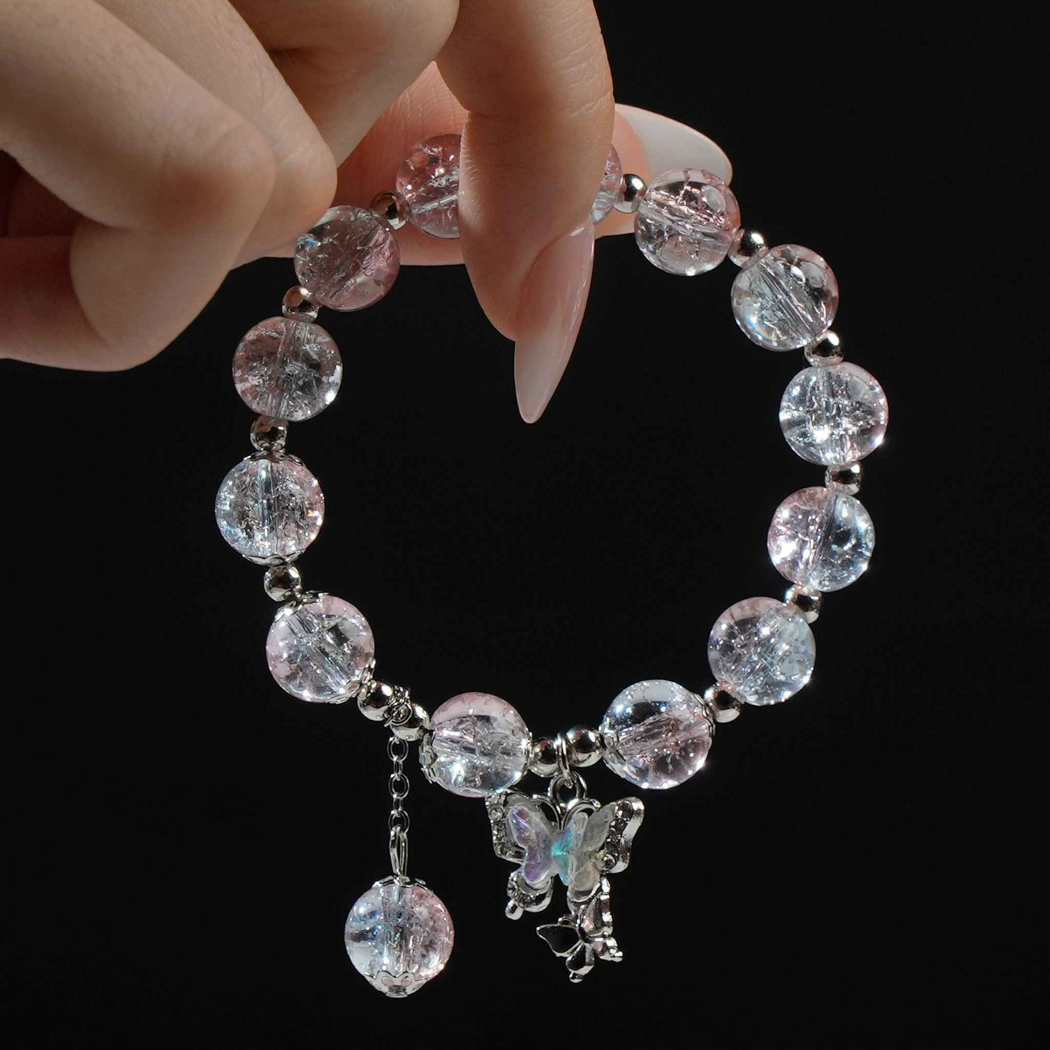 A translucent bracelet in soft pink and white tones, gently held in hand and embellished with a butterfly charm—romantic, dreamy, and delicately elegant.