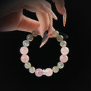 A close-up of a hand delicately holding a natural stone bracelet made of pink strawberry quartz and gray moonstone beads, showing sparkle and color contrast.