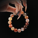 A hand gently holds a circular red hematoid quartz bracelet, revealing the stone's fiery internal textures and glossy finish under soft lighting.