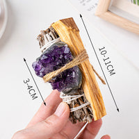 A hand holding a crystal-infused sage and palo santo bundle, showing size dimensions on a white background.