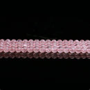Rows of polished rose quartz beads are laid out horizontally across the image, each bead reflecting subtle light. The image highlights the consistency in size and color, with gentle internal textures visible through the translucent surface.