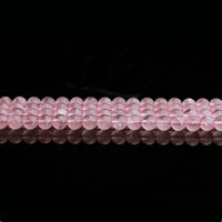 Rows of polished rose quartz beads are laid out horizontally across the image, each bead reflecting subtle light. The image highlights the consistency in size and color, with gentle internal textures visible through the translucent surface.