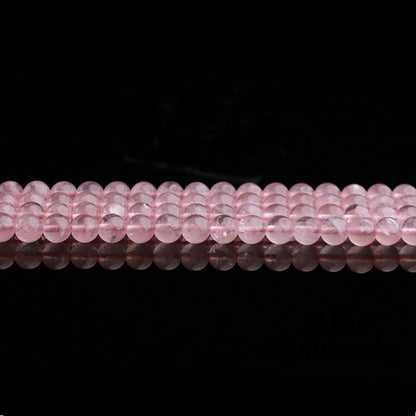 Rows of polished rose quartz beads are laid out horizontally across the image, each bead reflecting subtle light. The image highlights the consistency in size and color, with gentle internal textures visible through the translucent surface.
