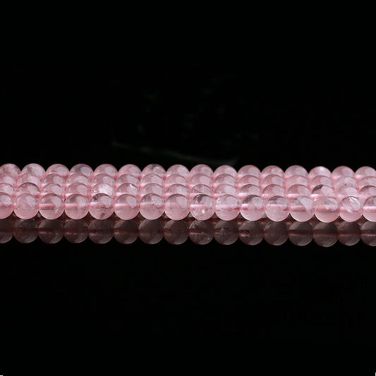 Rows of polished rose quartz beads are laid out horizontally across the image, each bead reflecting subtle light. The image highlights the consistency in size and color, with gentle internal textures visible through the translucent surface.