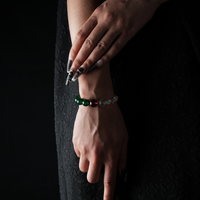 Hand wearing a bracelet composed of clear quartz, green agate, garnet, and a gold-tone spacer bead.