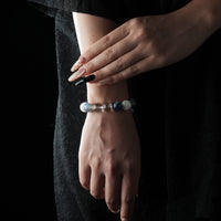 A bracelet made of moonstone, kyanite, and snowflake ghost quartz, shown on a wrist against a dark outfit.