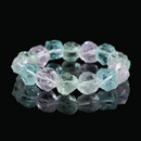 Close-up of a natural raw crystal bracelet, featuring irregular crystal shapes with shades of green, pink, and clear hues, reflecting light on a dark surface.