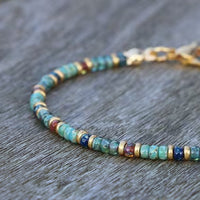 A detailed view of small turquoise and multicolor disc beads strung into an anklet with gold findings.