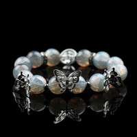 Handmade opalite energy bead bracelet with silver butterfly charms, radiating a mystical glow on a glossy black background.