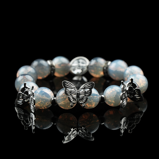 Handmade opalite energy bead bracelet with silver butterfly charms, radiating a mystical glow on a glossy black background.