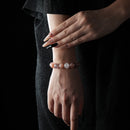 A beaded bracelet featuring orange moonstone, rose quartz, and strawberry quartz, worn on the wrist against a black outfit backdrop.