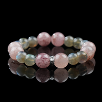 A beaded bracelet featuring strawberry quartz and gray moonstone beads, centered with a silver charm, displayed on a reflective black surface.