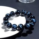 Bracelet styled on a white dish under sunlight, with vivid blue-black chatoyant patterns and polished finish.