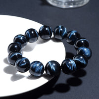 Bracelet styled on a white dish under sunlight, with vivid blue-black chatoyant patterns and polished finish.