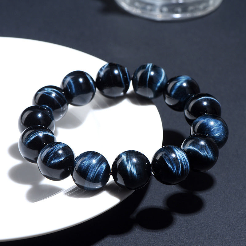 Bracelet styled on a white dish under sunlight, with vivid blue-black chatoyant patterns and polished finish.