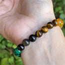 A beaded crystal bracelet worn outdoors, catching natural light to highlight the golden and green hues of the stones.