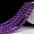 This image displays strands of dark purple beads hanging gracefully from a textured white ceramic bowl. The contrast between the glossy beads and the rough ceramic adds visual interest against the plain black background.