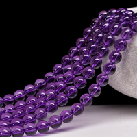 This image displays strands of dark purple beads hanging gracefully from a textured white ceramic bowl. The contrast between the glossy beads and the rough ceramic adds visual interest against the plain black background.