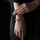 A delicate rose quartz beaded bracelet with a silver heart charm, worn on the wrist, styled with a black outfit.