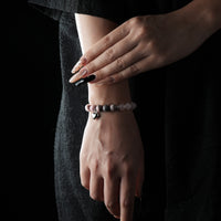 A delicate rose quartz beaded bracelet with a silver heart charm, worn on the wrist, styled with a black outfit.
