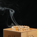 Side angle of bracelet on bamboo smudging box, smoke spiraling in background.