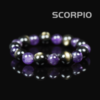 Flat lay of Scorpio zodiac bracelet featuring deep purple amethyst, metallic hematite, and gold-toned pyrite on a black reflective surface.