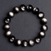 A silver sheen obsidian bracelet placed on a gray background, with noticeable contrast between black beads and silver luster.